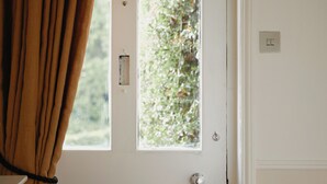 A white door with a window, a visible light switch, and a curtain partially drawn to the side. - Trinity Farmhouse-Stunning House&Garden (Cirencester)
