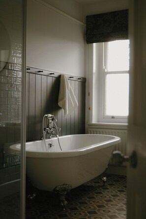 Une salle de bain avec une baignoire sur pieds, une fenêtre agrémentée d’une lambrequin et un sol carrelé.