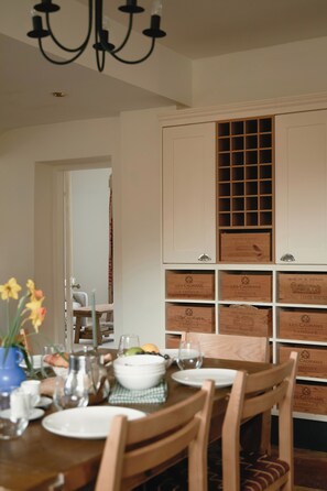 Un coin repas avec une table en bois dressée pour deux personnes, entourée de chaises. On peut voir des caisses à vin accrochées au mur derrière la table.
