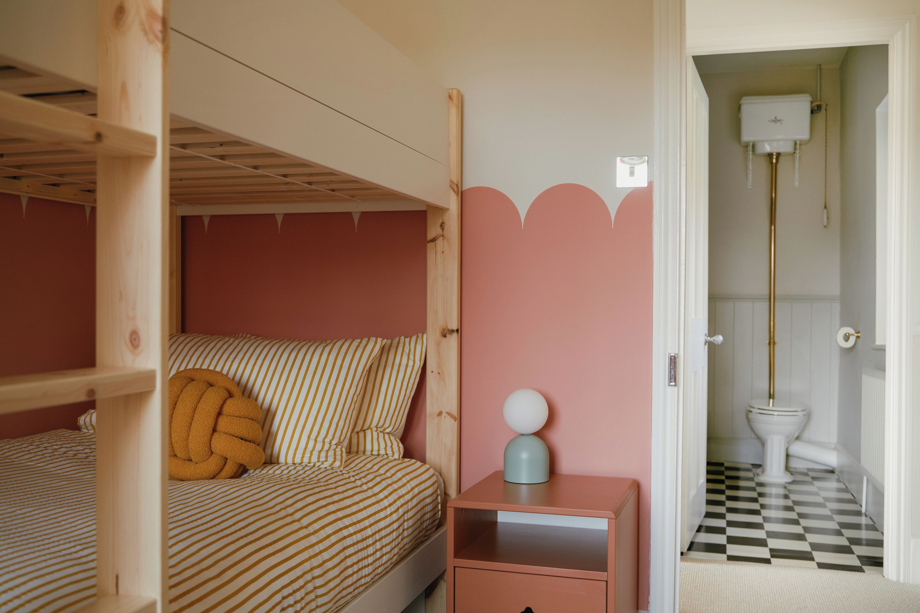 Ein Schlafzimmer mit Etagenbett, Nachttisch mit Lampe und einer rosa Wand mit geschnitzter Verzierung.