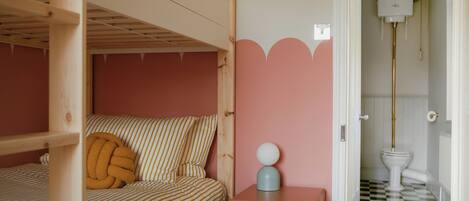 Ein Schlafzimmer mit Etagenbett, Nachttisch mit Lampe und einer rosa Wand mit geschnitzter Verzierung.