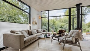 A modern living room with a large window, a sofa, a coffee table, and a fireplace. - Cozy home in Hornbæk with WiFi (Hornbæk)