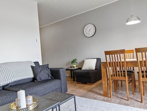 A living room with a sofa, a coffee table, a dining table with chairs, a clock on the wall, and a potted plant.