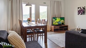 Et værelse med spisebord, stole, sofa, tv og udsigt til det fri.