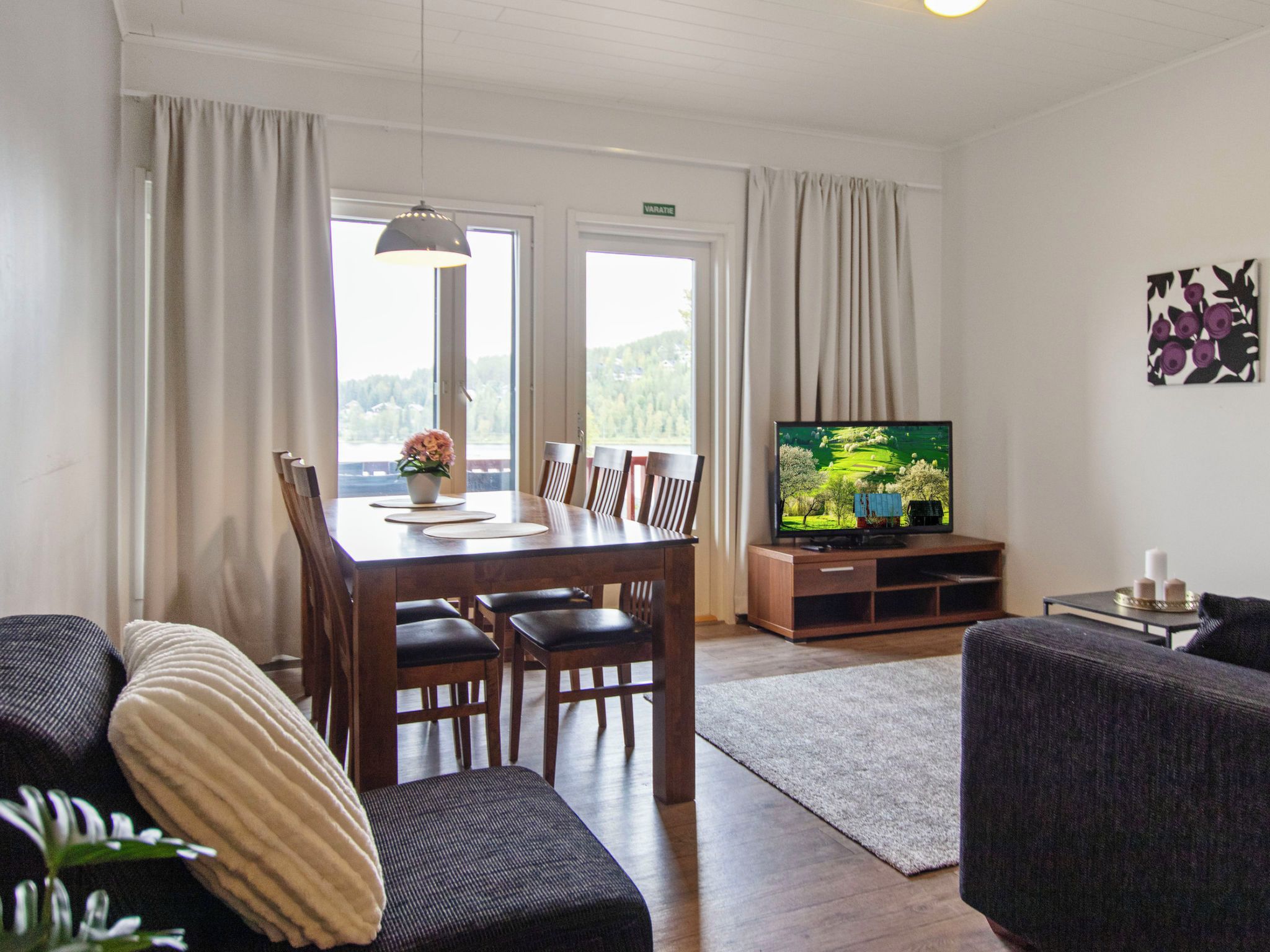 Een woonkamer met een eettafel, stoelen, een bank, een televisie en uitzicht op het groen.