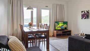 Een woonkamer met een eettafel, stoelen, een bank, een televisie en uitzicht op het groen.