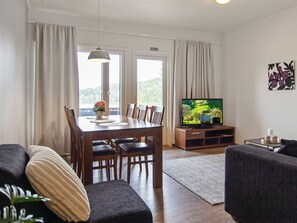 A living room with a dining table, chairs, a sofa, a TV, and a view of the outdoors. - Skivillas 47 ukkohalla (a8) by Interhome (Hyrynsalmi)