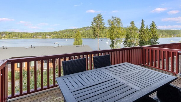 En terrasse med et bord og stole med udsigt over en sø med både og huse i baggrunden.