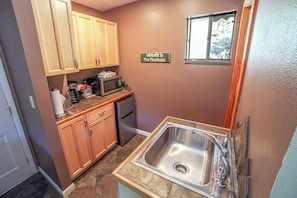 A compact kitchen with wooden cabinets, a microwave, a coffee maker, and a stainless steel sink.