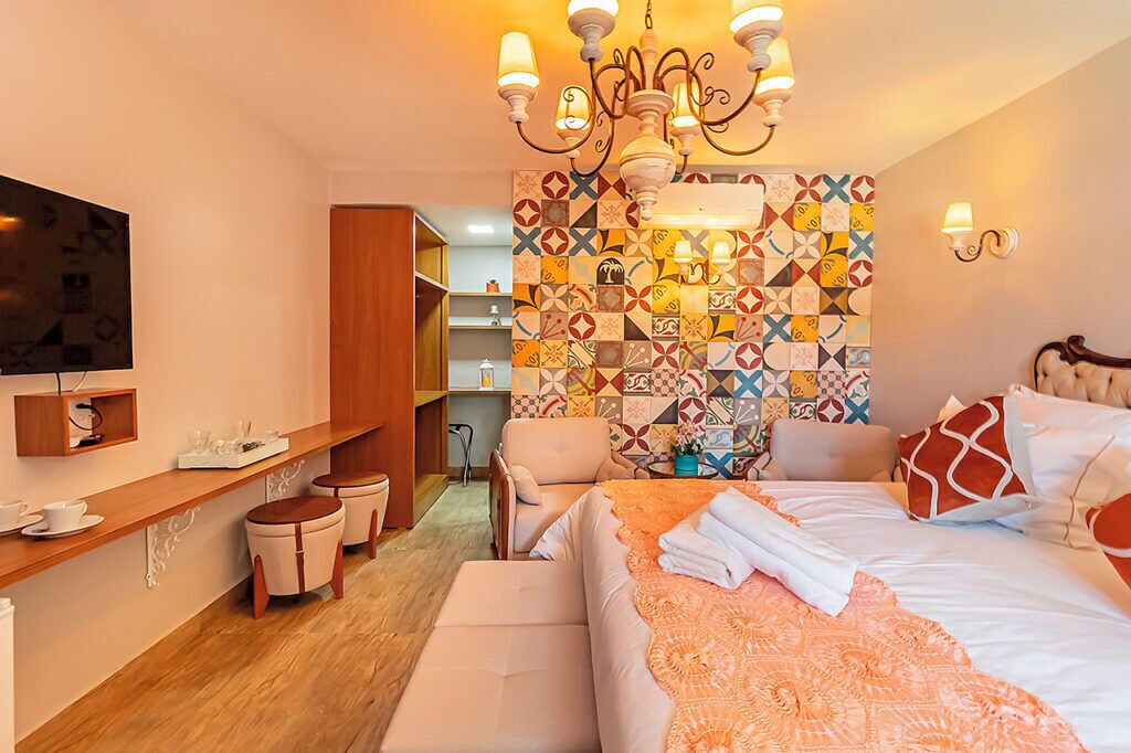 A hotel room with a bed, a TV, a wooden desk, and a colorful tiled wall.
