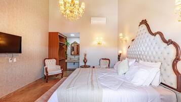 A bedroom with a large bed, a chandelier, a television, and a wooden bench.