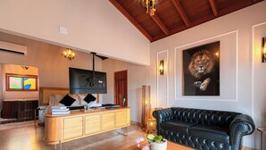 A living room with a wooden coffee table, a black leather sofa, a mounted television, and a large framed artwork of a lion. - Pousada Vila Rica (Pirenópolis)