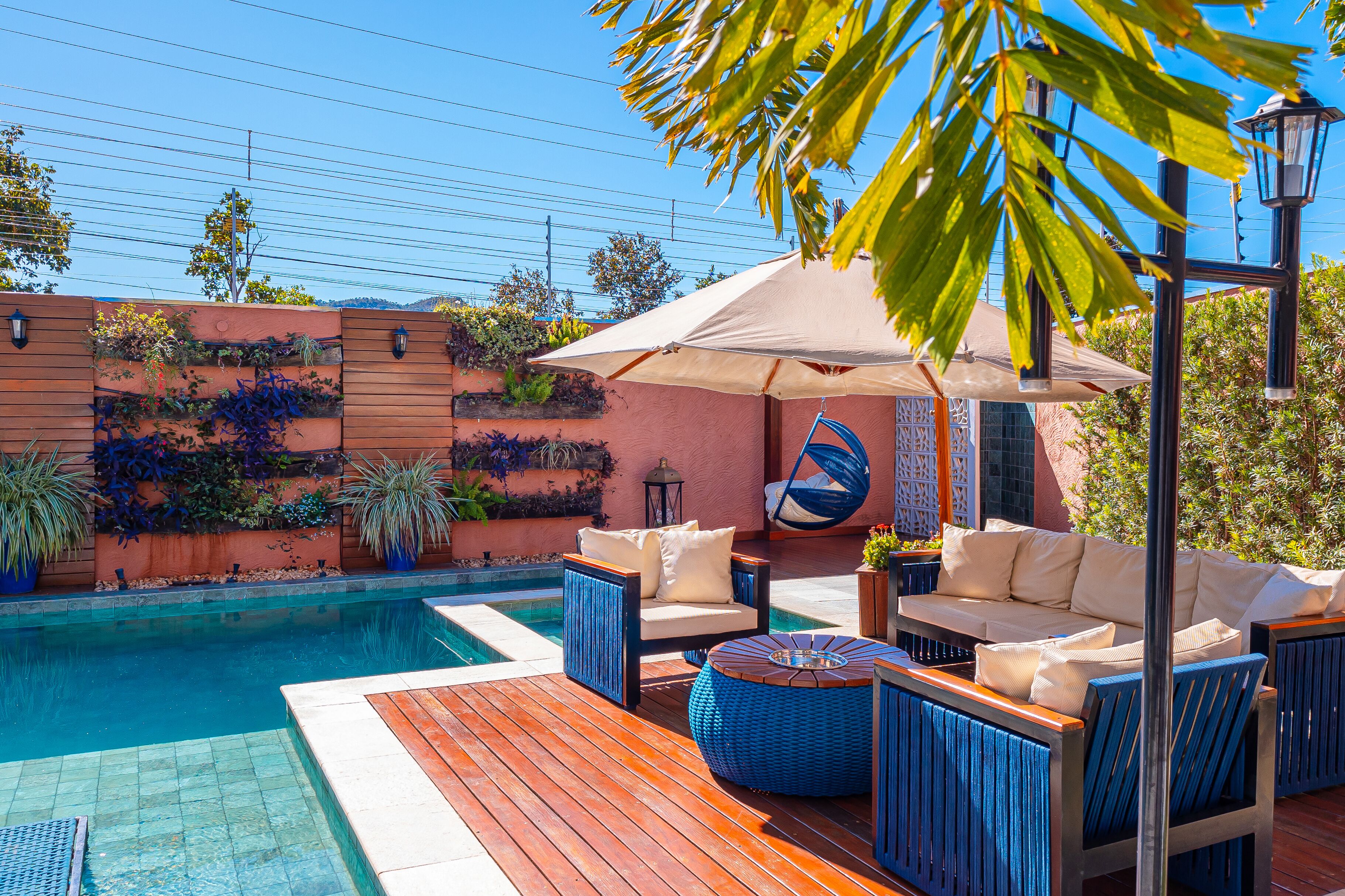 Zona junto a la piscina con cubierta de madera, mobiliario exterior y una pérgola con sombrilla.