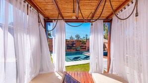 A covered outdoor seating area with a pool view, wooden flooring, and white curtains. - Pousada Vila Rica (Pirenópolis)