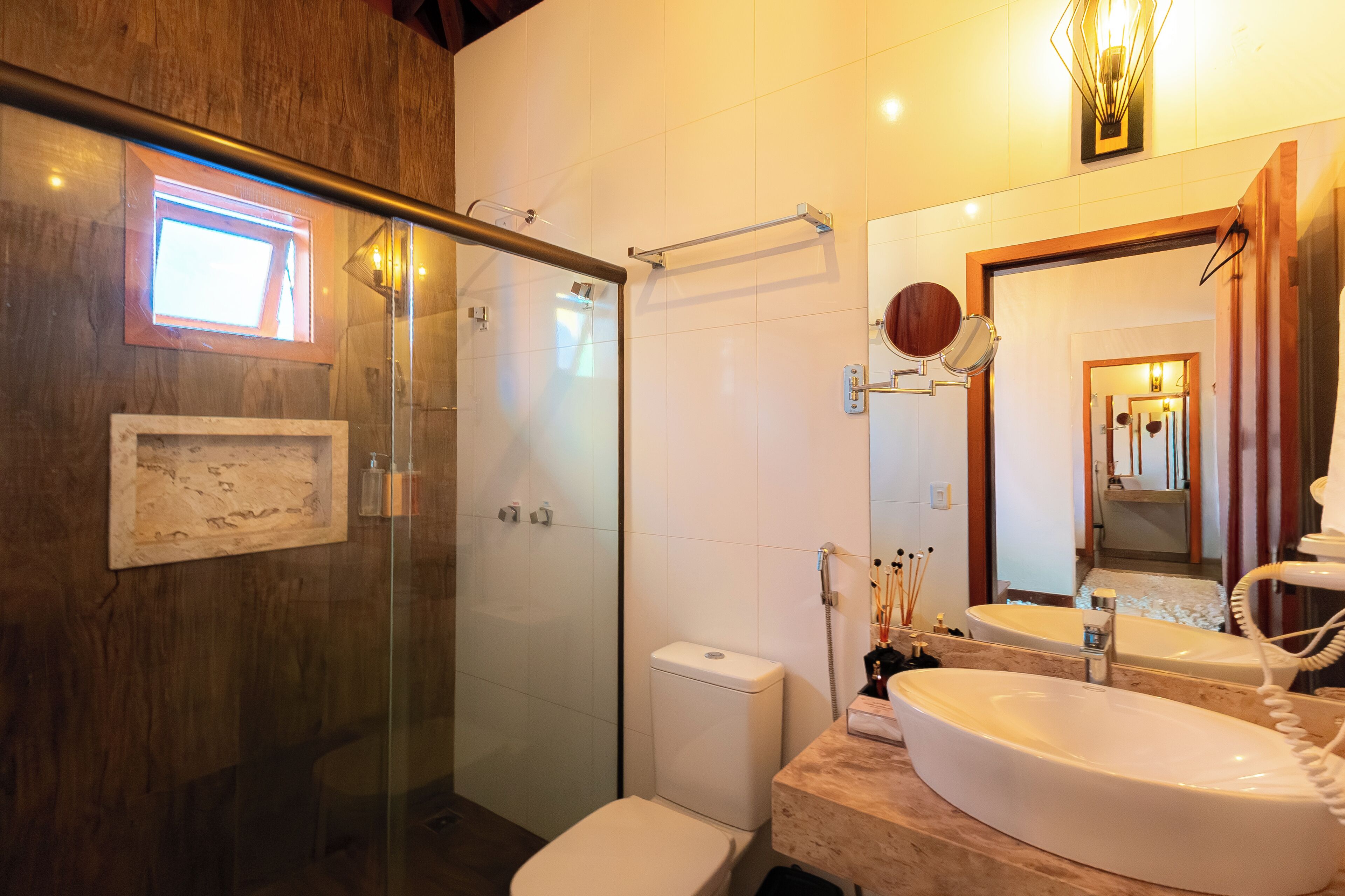 Een badkamer met een glazen douchecabine, een toilet, een wastafel met spiegel en een lijst met een afbeelding aan de muur.