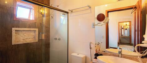 Een badkamer met een glazen douchecabine, een toilet, een wastafel met spiegel en een lijst met een afbeelding aan de muur.