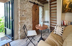 Una sala de estar acogedora con una pared de piedra, una puerta de madera, una pequeña mesa con una silla, una estantería y un sofá con cojines estampados.