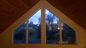 A room with a sloped wooden ceiling and a large triangular window. - Charming AFrame home w/2BR, 2BA, office suite, AC, WiFi & outdoor living (Keaau)