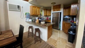 A modern kitchen with wooden cabinets, a stainless steel refrigerator, and a granite countertop. - Charming AFrame home w/2BR, 2BA, office suite, AC, WiFi & outdoor living (Keaau)