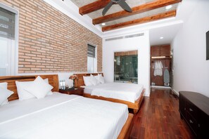 Two single beds with white linens and wooden headboards, a nightstand, and a lamp, set against a brick accent wall.