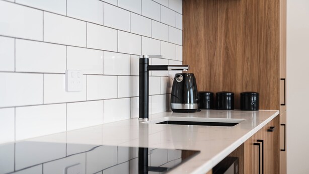 A kitchen with a white tiled backsplash, a black faucet, a coffee maker, and black condiment containers on the counter. - Premium Living on Stuart Street (Dunedin)