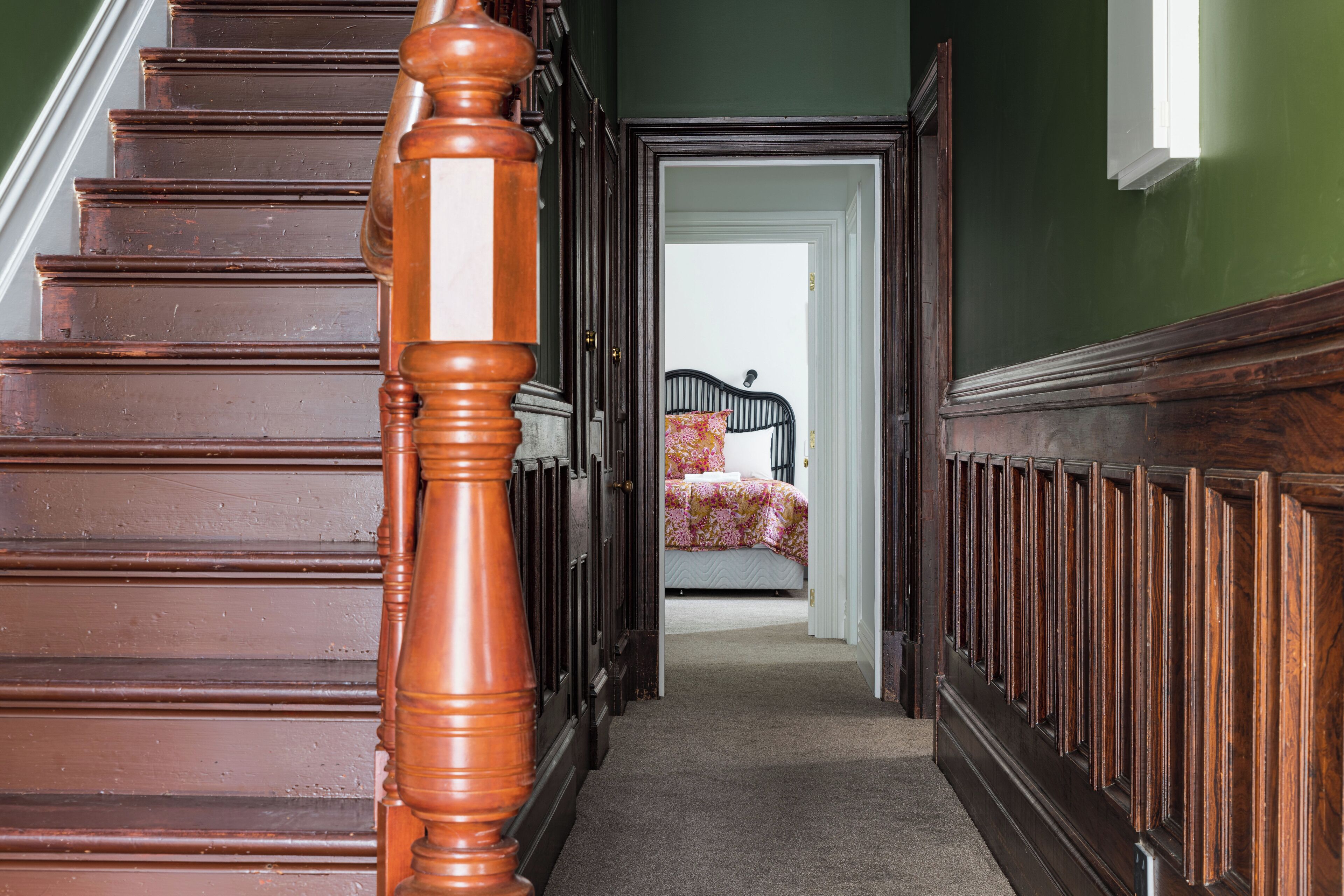 A wooden staircase leading to a bedroom with a bed and a nightstand.
