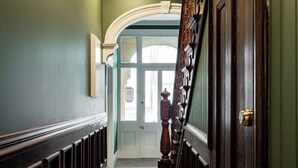 A hallway with a wooden staircase, a door with a brass doorknob, and a light-colored carpet. - Premium Living on Stuart Street (Dunedin)