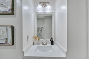 A modern bathroom with a white sink, a large mirror, and a light fixture above the mirror.