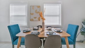 Un coin repas avec une table en bois, des chaises recouvertes d’un tissu bleu et un vase contenant des plantes séchées.