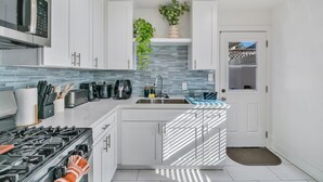 Une cuisine moderne avec des armoires blanches, un four à micro-ondes en acier inoxydable, une cuisinière à gaz et un évier. Deux plantes en pot sont posées sur le plan de travail.