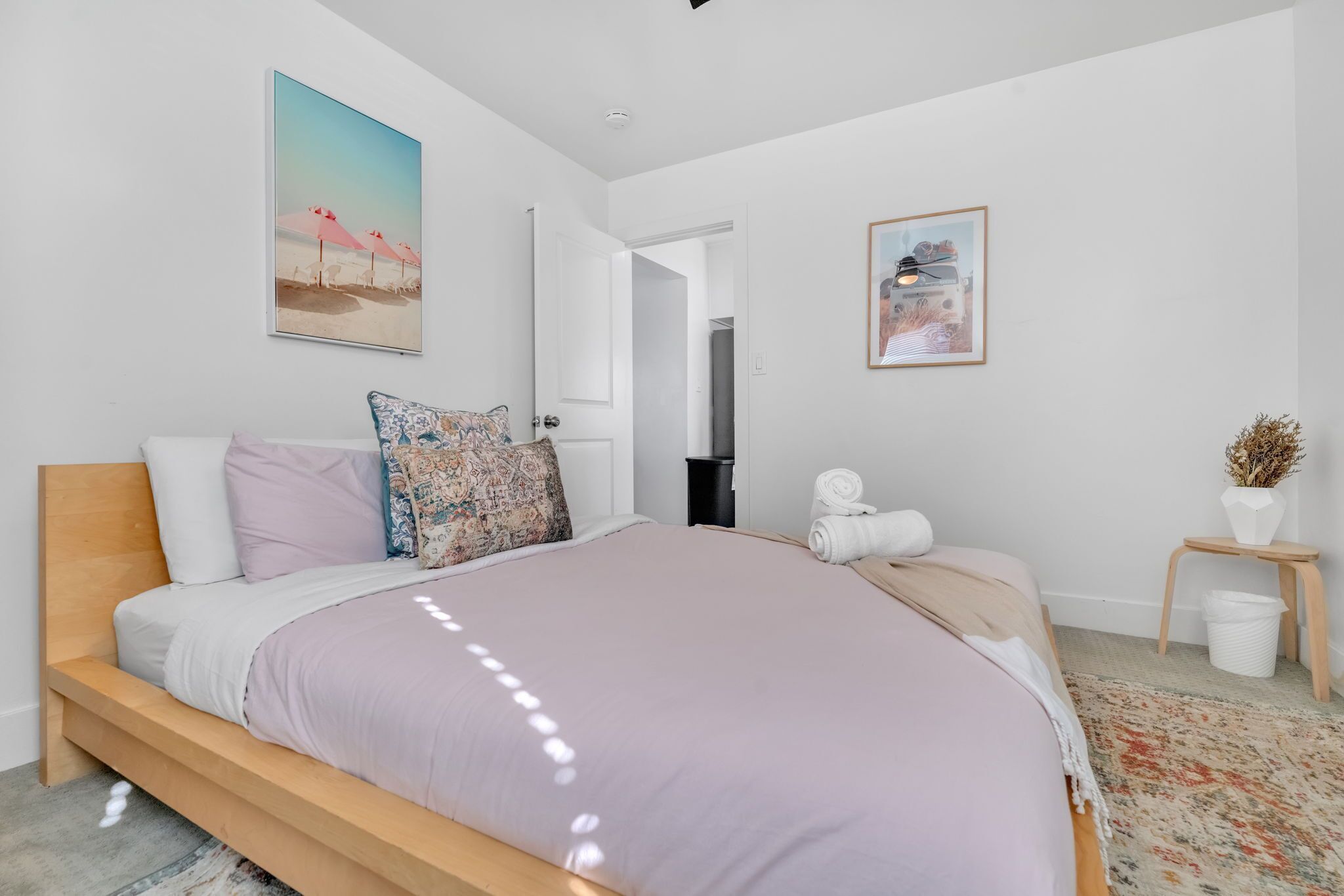 Un dormitorio moderno con una cama grande, cabecera de madera, almohada estampada y un cuadro enmarcado en la pared.