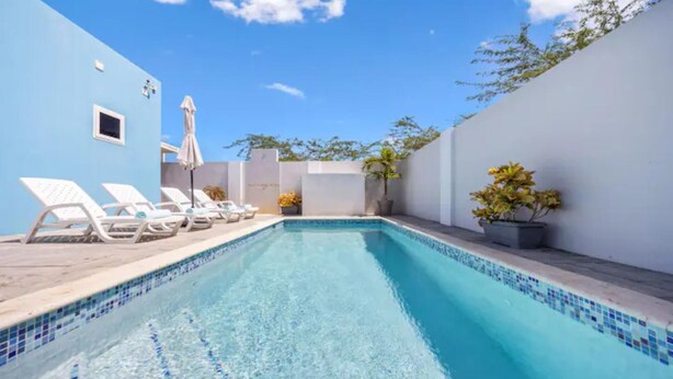 Una piscina con agua cristalina, rodeada de paredes blancas y un cielo azul.