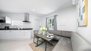 Una cocina moderna con armarios blancos, una mesa de comedor con sillas y un sofá gris.