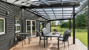 A covered outdoor patio with a wooden deck, a table with chairs, and a grill.