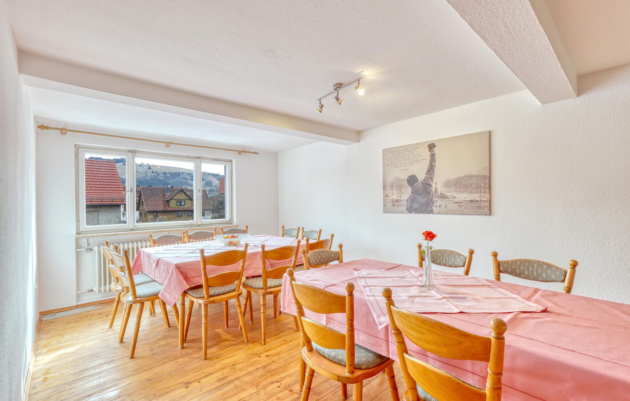 A dining area with a long table, multiple chairs, and a view of a village through a window.
