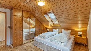 A bedroom with a sloped ceiling, wooden paneling, a skylight, a bed with white linens, a bedside table with a lamp, and a wardrobe. - Beautiful apartment in Bischofsheim (Bischofsheim)