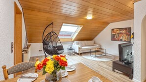 A cozy loft apartment with a wooden ceiling, a hanging chair, a white sofa, a dining table with a vase of flowers, and a television. - Beautiful apartment in Bischofsheim (Bischofsheim)