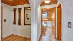 A hallway with wooden flooring, white textured walls, and wooden ceiling beams. There are three mirrors on the wall and a door leading to a bathroom. - Beautiful apartment in Bischofsheim (Bischofsheim)