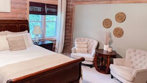 Ein Schlafzimmer mit einem großen Bett, zwei Sesseln, einem kleinen Tisch und einem Fenster mit Jalousien.
