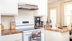 A modern kitchen with white cabinetry, a stainless steel range hood, a coffee maker, and a countertop with a book and a bottle. - Lake O' The Pines Lake Front
Two Bedroom Home - A Slice of Paradise (Jefferson)