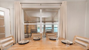 A dining area with a wooden table, six chairs, and a view of the sea through large windows. - Lake O' The Pines Lake Front
Two Bedroom Home - A Slice of Paradise (Jefferson)