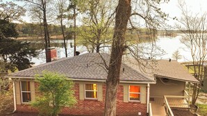 A single-story brick house with a sloped roof, a small porch, and a view of a lake. - Lake O' The Pines Lake Front
Two Bedroom Home - A Slice of Paradise (Jefferson)