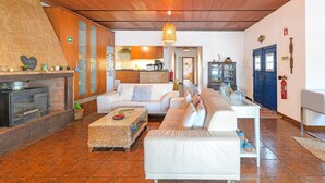 A living room with a fireplace, white sofas, a kitchen in the background, and a blue door. - Cottage 'Olive Village Alentejo' with Private Pool, Wi-Fi and Air Conditioning (Vila Azedo)