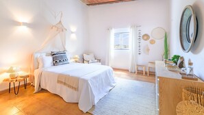 A bedroom with a bed, bedside tables, a nightstand, a window with curtains, a wooden ceiling, and a wall-mounted mirror. - Cottage 'Olive Village Alentejo' with Private Pool, Wi-Fi and Air Conditioning (Vila Azedo)