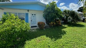Una casa con puerta y ventanas azules, rodeada de un césped cuidado y diversas plantas.