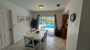 Un comedor con mesa y sillas, vistas a una piscina y una cocina con armarios y un reloj.