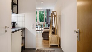 Ein schmaler Flur führt zu einem Wohnbereich mit einer Couch, einem Couchtisch und einem Fenster mit Vorhängen.