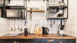 A kitchen with a microwave, toaster, kettle, and various utensils on shelves.