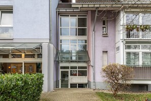 Un bâtiment avec une entrée en verre, une enseigne portant le numéro 59 et un petit arbre devant.