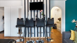 Moderni olohuone, jossa on raidalliseen seinään asennettu televisio, neljä mustaa baarituolia, harmaa sohva ja turkoosinsävyinen korosteseinä.